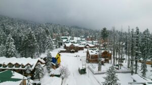 A picturesque winter scene in Gulmarg showing snow-covered buildings and coniferous trees.